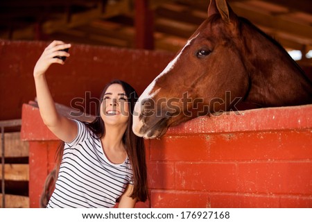 Beautiful young Hispanic woman taking a photo of herself and her horse at the stables