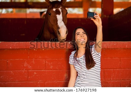 Cute young brunette taking a selfie with his horse in the stables