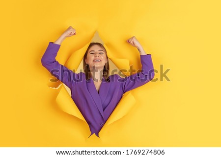 Happy winner. Cheerful caucasian young woman poses in torn yellow paper background, emotional and expressive. Breaking on, breakthrought. Concept of human emotions, facial expression, sales, ad.