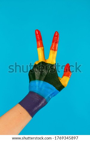 close-up hand painted as rainbow flag shows victory gesture on a blue background.  LGBT topics, lesbians, gays, transgender, bisexual.  