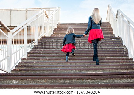 Beautiful mother blonde with red lipstick with a small daughter spend time together, walk, sit run on the stairs. They look at the camera, hug and laugh. The theme of motherhood and pastime of mothers