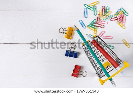 Paper clips in shopping cart on white wooden background