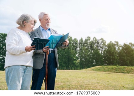 Portrait of a gray haired senior Caucasian people holding a folder with documents on the background of nature in the park. Elderly married couple