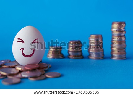 Faces on the eggs, investment concept. Happy investor smiling in front of his growing money. Blue background with stacks of coins