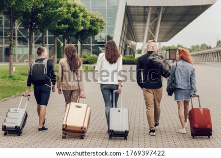 Rear view of positive young people with luggage outdoor. Friends go to the airport to fly on vacation Royalty-Free Stock Photo #1769397422