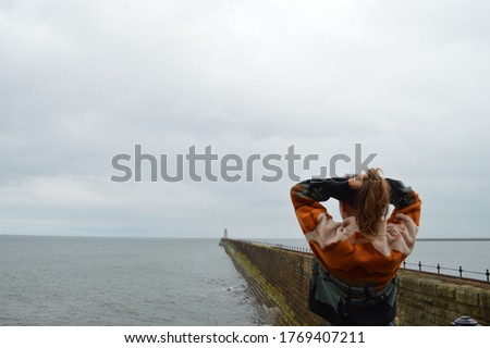 Woman in adventurous jumper looking out at sea. Lighthouse in the background. Landscape.