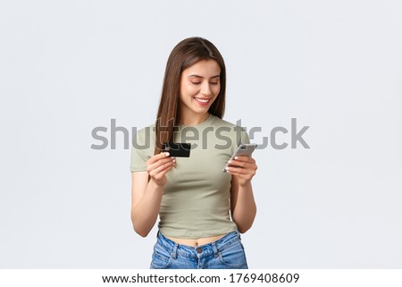 Online shopping, home lifestyle and people concept. Smiling attrctive woman purchase items in internet store, using credit card to pay with mobile phone, standing white background Royalty-Free Stock Photo #1769408609