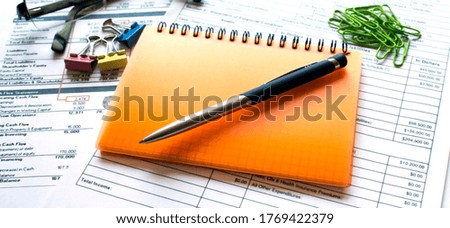 Orange notebook and glasses, clip paper on on financial tables