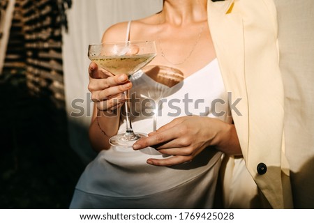 Luxurious woman wearing a white dress, holding a coupe with champagne in sun light. Concept of an open air party. Royalty-Free Stock Photo #1769425028