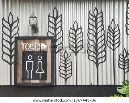 Toilet direction sign on the zinc sheet wall with beuatiful pattern ear of rice and the lamp.