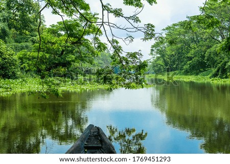 A landscape of a river with transparent water flowing through a village with surrounding greenery captured from a boat. Blue sky above with its reflection on the water