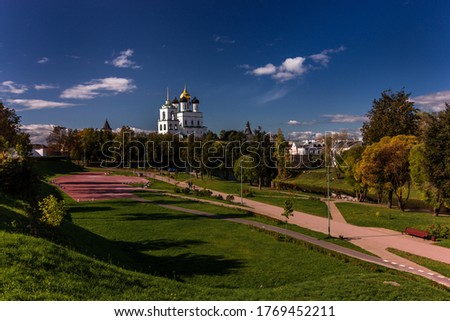View of the Pskov Kremlin over the bridge at the city river on a summer clear day. The blue bright sky with clouds is reflected in a smooth surface of water.