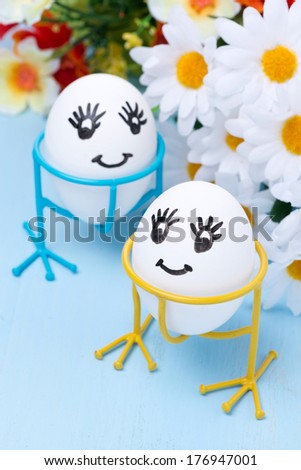 two funny smiling eggs on stands and flowers for Easter, selective focus, vertical