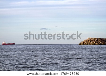 The seawall around the sea port facilities is made of concrete tetrapods (traveling-wave protection), rubble-mound breakwater and the tanker on the roadstead Royalty-Free Stock Photo #1769495960