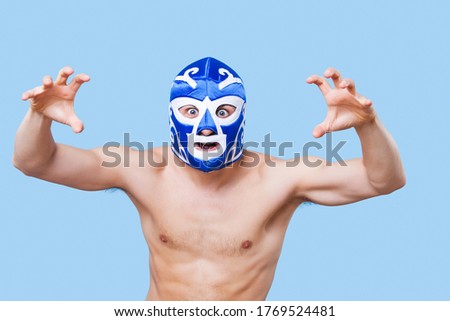 Portrait of shirtless man in wrestling mask gesturing over gray background