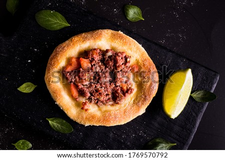 Legitimate Arabic sfiha meat on black cutting board and lemon cut in half on black background Royalty-Free Stock Photo #1769570792