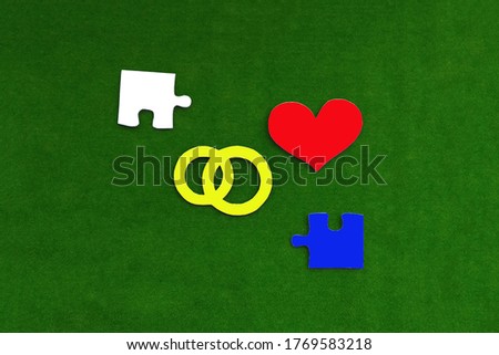 Red heart, wedding rings, a pair of puzzles in blue and white on a green background. Marriage, spouses, love.