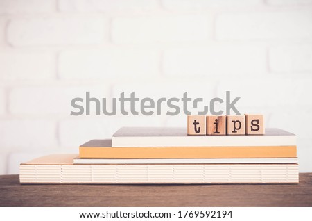 The word TIPS, letters on wooden block cubes on top of books and table with white bricks background,  blank copy space, vintage minimal style. Concepts of  tricks, hack, help, guideline, useful hint. Royalty-Free Stock Photo #1769592194