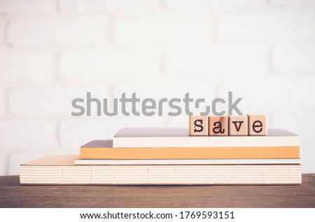 The word SAVE, alphabets on wooden rubber stamps on top of books with white bricks background, blank copy space, vintage minimal style. Concepts of budget management, bank, financial or protect.