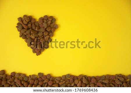 Dried cat food with heart shape as an abstract background texture on yellow background. Flat lay, copy space. Pet shop poster design, useful for zoo shop, pets care, food and goods for animals.