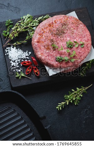 Raw fresh serbian pljeskavica or spiced meat patty mixture of pork and beef, vertical shot on a black stone surface
