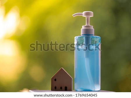 Hand sanitizer bottle with wooden house model, blurred background, COVID-19 Coronavirus concept.