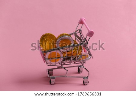 Shopping theme. Mini Supermarket trolley with coins on pink background.