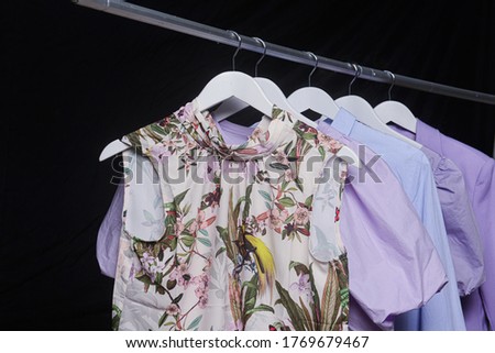 Female floral ,palm pattern dress and blue shirt and purple sundress, blouse on hanger-black background


