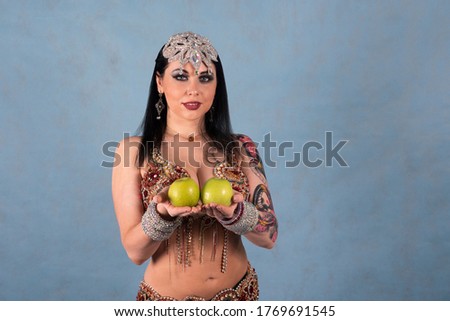 A beautiful Oriental dancer poses in the Studio on a blue background with two green apples