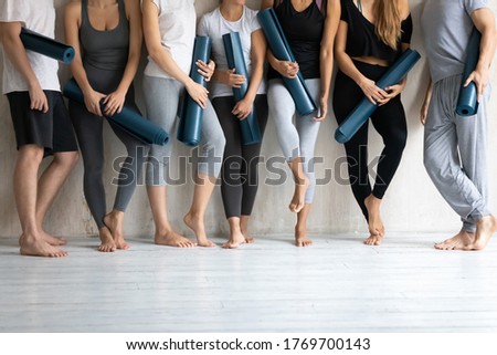 Group of young fit multiethnic people with individual rubber mats standing barefoot near wall, relaxing after intensive workout or waiting for yoga lesson or educational seminar in modern loft studio. Royalty-Free Stock Photo #1769700143