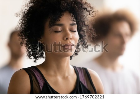 Head shot close up young peaceful attractive curly hair african american woman breathing fresh air, enjoying deep meditation with closed eyes, relaxing after yoga class workout in sport club. Royalty-Free Stock Photo #1769702321