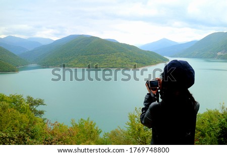 Female hiker taking photo of the scenic panoramic view of Jinvali water reservoir, Aragvi river, Georgia