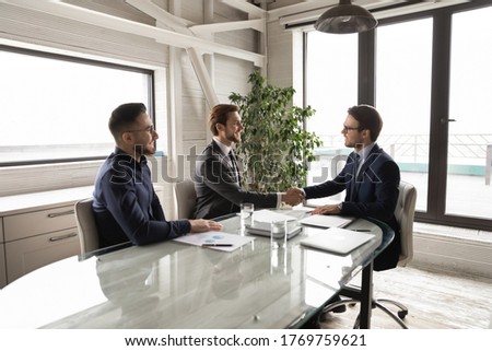 Smiling businessmen shake hands closing deal after successful negotiations in office, happy multiracial male business partners handshake get acquainted greeting at meeting, partnership concept