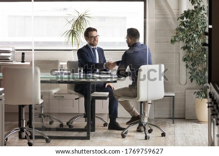 Smiling multiracial young businessmen handshake greeting get acquainted at boardroom briefing, excited diverse male business partners shake hands make agreement after successful office negotiations Royalty-Free Stock Photo #1769759627