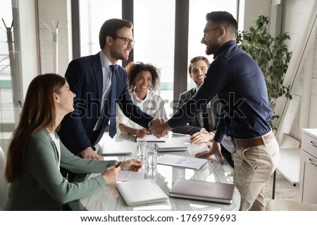 Smiling multiethnic male business partners shake hands close deal make agreement at team meeting in boardroom, excited diverse businessmen handshake get acquainted greeting at briefing in office Royalty-Free Stock Photo #1769759693