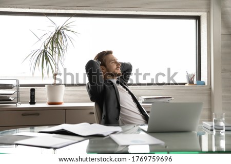 Happy young male boss relax lean back in chair in office look in distance dreaming or thinking, calm Caucasian businessman rest at workplace, breathe fresh air, take break, stress free concept Royalty-Free Stock Photo #1769759696