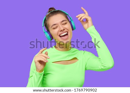 Close up portrait of teen girl singing and dancing while listening to music in wireless headphones, isolated on purple background