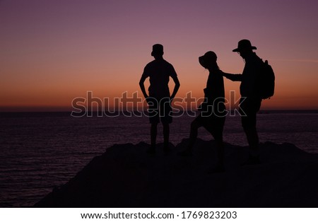 Silhouette of family standing on rock near sea at sunset.