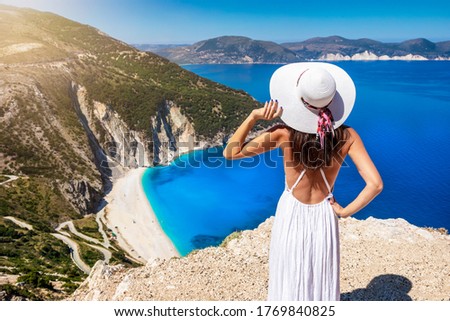A beautiful tourist woman in white dress and sunhat enjoys the view to the famous Myrtos Beach on the island of Kefalonia, Ionian Sea, Greece Royalty-Free Stock Photo #1769840825