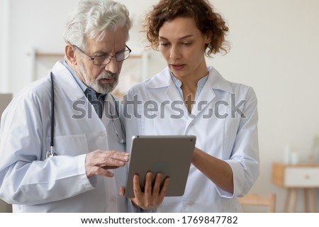 Concentrated man and woman doctors in white medical uniforms look at tablet screen discuss patient anamnesis or checkup results together, diverse GP talk brainstorm make decision using pad gadget Royalty-Free Stock Photo #1769847782