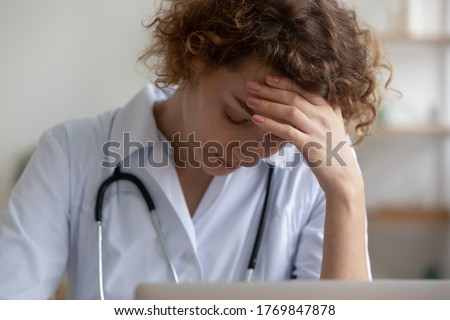 Upset tired young Caucasian female nurse feel frustrated distressed with overwork late hours in hospital, stressed woman doctor or GP suffer from headache or migraine, have hard working day in clinic