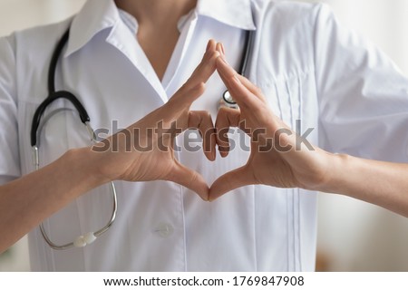 Crop close up of female doctor in white medical uniform show heart love sign or gesture, demonstrate care support hospital patient needs, woman nurse use nonverbal language, healthcare concept