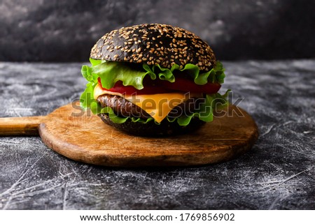Black burger with sesame seed black bun, beef meat cutlet, cheese and vegetables on wooden rustic cutting board background. Close up. Selective soft focus. Shallow depth of field. Text copy space.