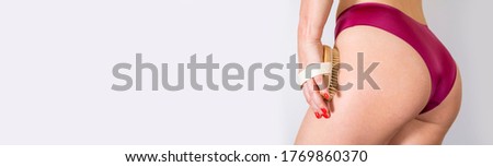 Health, people, bodycare and beauty concept. Close up of woman buttocks with cellulite in red silk panties. Young woman holding brush in her hand anti-cellulite treatment. Cellulite problem