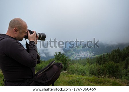 Male photographer taking a picture using professional DSLR while hiking in the Swiss Alps near Lauterbrunnen and Wengen in the Jungfrau Region on a foggy day. Switzerland