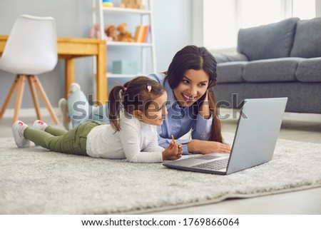 Happy mother and her cute little daughter watching online entertainment video together on laptop at home