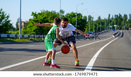 Basketball family, father with beard and son playing fearless basketball in middle of road among cars