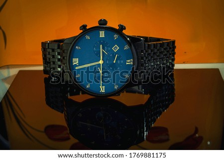 A blue dial watch on a glassy surface with orange background.