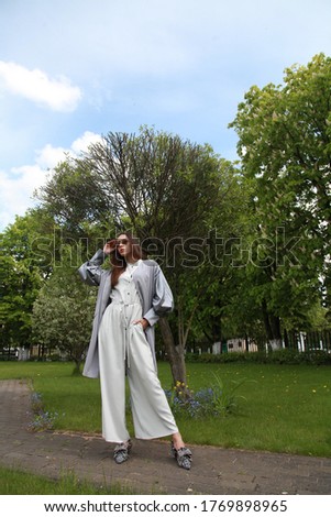 Beautiful brunette woman natural make up wear fashion clothes casual dress code office style grey jacket and pants suit for romantic date business meeting. City park with green trees background