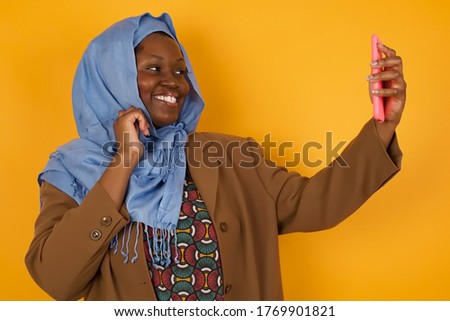 Portrait of a pretty happy African American muslim girl taking a selfie isolated over bright background